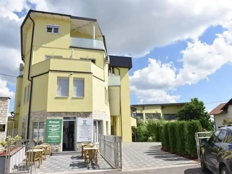 Zgrada Gold Apartmana u Kozarcu: žuta fasada, balkoni, terasa i parking ispred